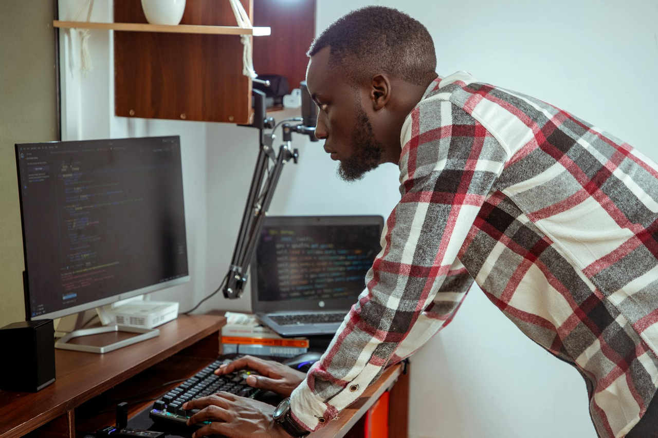 Focused IT specialist in casual attire working at a computer in a modern office setting.